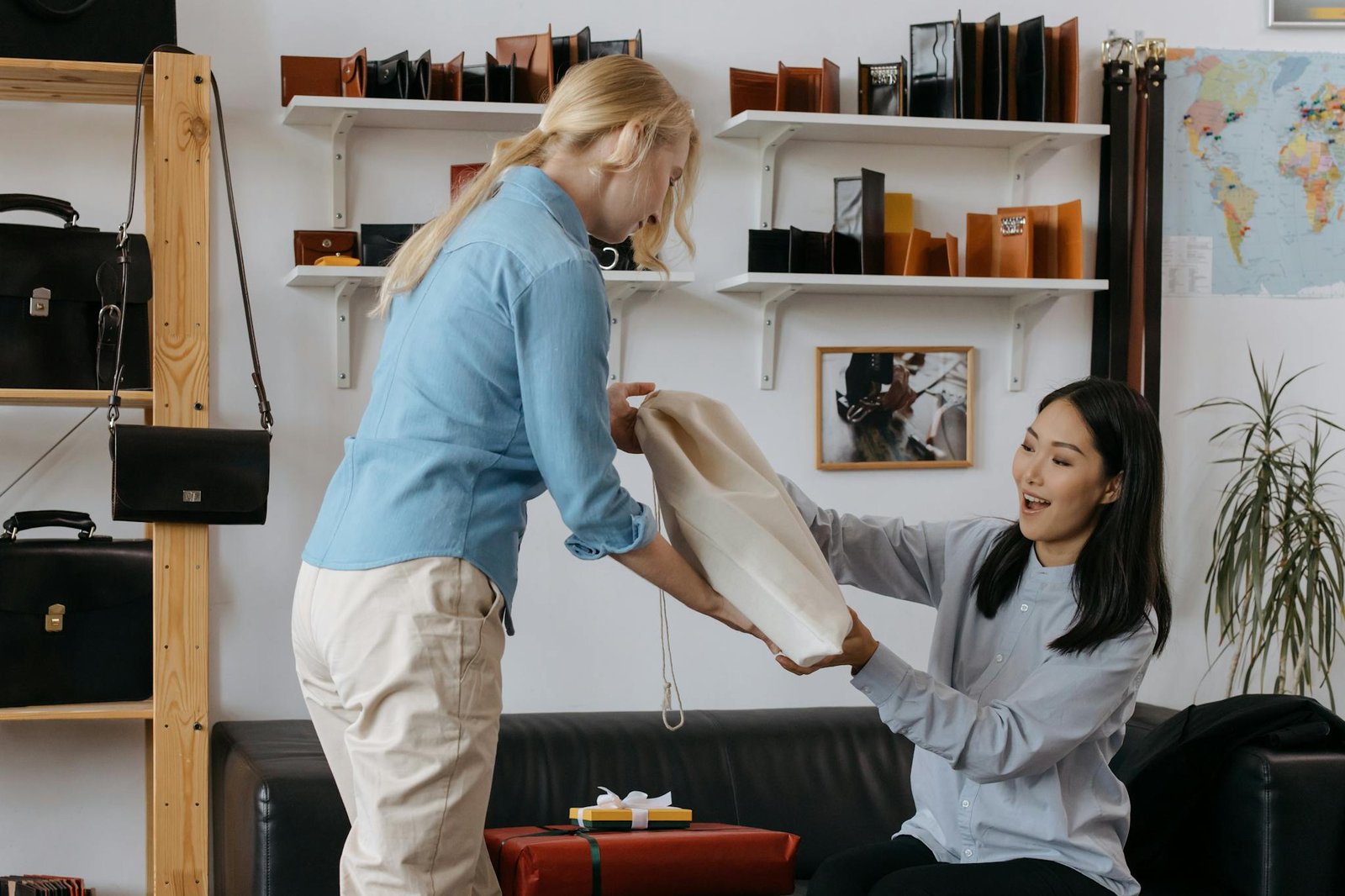 Two women in a leather goods store, one giving a bag to the other, surrounded by shelves of bags.